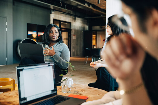 Businesswoman communicating with team while sitting at startup workspace