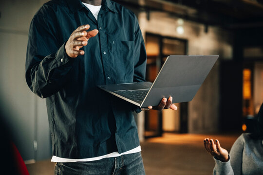 Midsection of male entrepreneur holding laptop and giving presentation to team at office