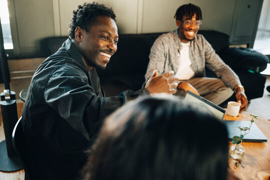 Happy male entrepreneur interacting with coworkers while discussing ideas at office