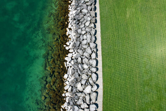 Aerial view of the rocky shoreline of Lake Geneva with turquoise water and a lush green lawn Morges, Vaud, Switzerland.