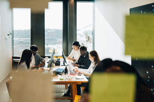 Group of diverse computer programmers working together while sitting around table at creative workspace