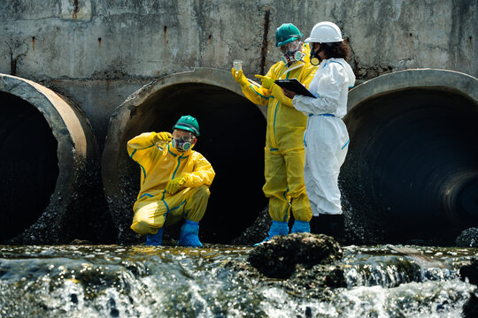 Hazmat workers in protective suits inspecting polluted wastewater drainage tunnel and contaminated industrial water during environmental hazard response operation