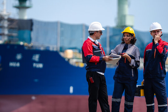 Industrial engineering team in safety helmets discussing operations and logistics management at shipping port with cargo vessel background and teamwork concept