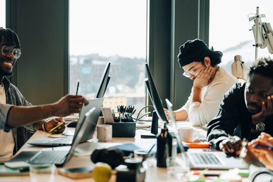 Group of male computer programmers working together while sitting around cluttered desk in office