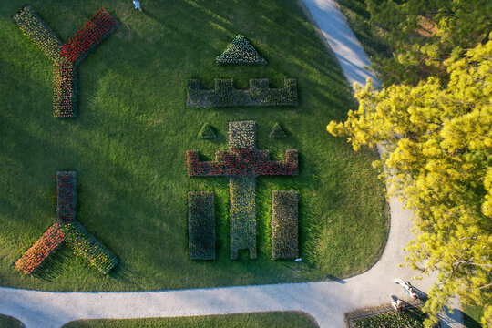 Aerial view of colorful flower beds shaped like a castle and letters in a green park with gravel paths and people walking Morges, Vaud, Switzerland.