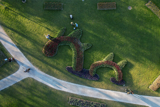 Aerial view of colorful flower beds in abstract shapes with people walking on paths in a green park in Morges, Vaud, Switzerland.