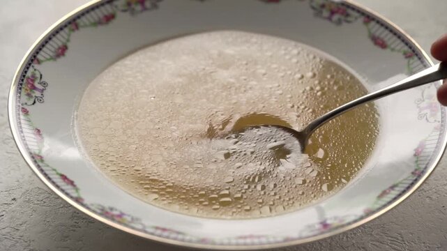 Stirring bone broth or soup in a plate with a spoon