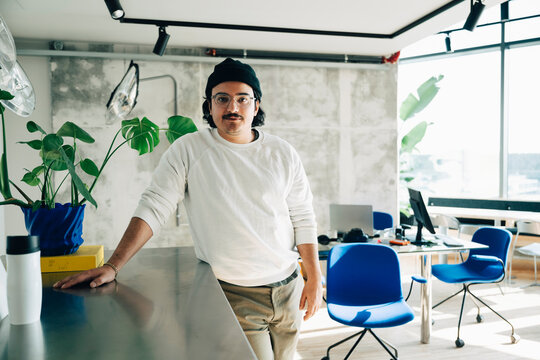 Portrait of male business professional leaning on table at modern workspace