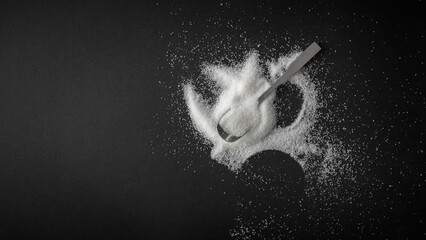 Top view of spilled sugar scattered across deep black background, creating striking contrast and minimalist composition. Large empty copy space for product placement or advertising text.  © magdal3na