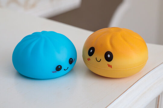 blue and yellow kawaii squishy dumpling toys with cute smiley faces and rosy cheeks placed side by side on white table surface