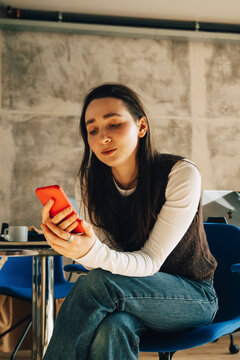 Young businesswoman scrolling smart phone while sitting on chair at office