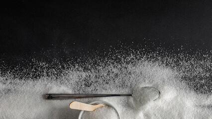 Top view of spilled sugar scattered across deep black background, creating striking contrast and minimalist composition. Large empty copy space for product placement or advertising text.  © magdal3na