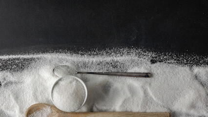 Top view of spilled sugar scattered across deep black background, creating striking contrast and minimalist composition. Large empty copy space for product placement or advertising text.  © magdal3na