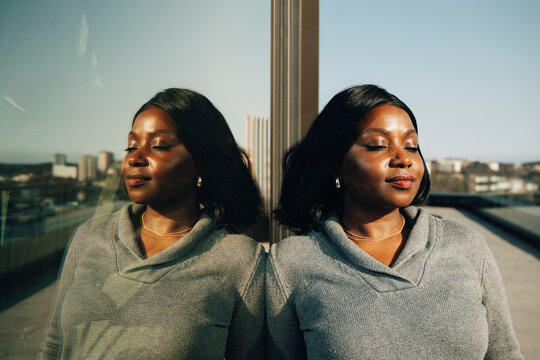 Businesswoman with eyes closed leaning on glass wall in office balcony