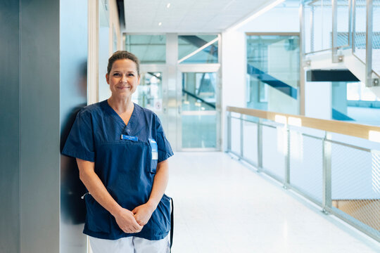 Portrait of smiling female healthcare worker standing near wall in hospital corridor