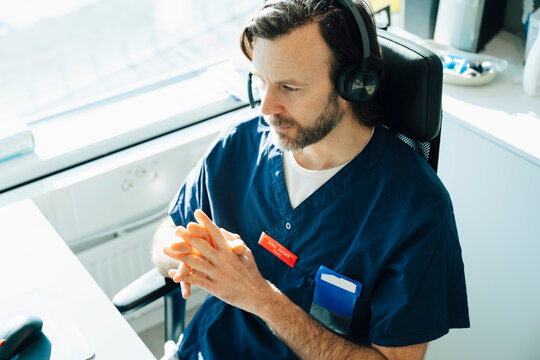 High angle view of male medical professional wearing headset attending video call while sitting in hospital office
