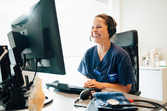 Happy female physician wearing headset consulting through video call on computer while sitting in office at hospital