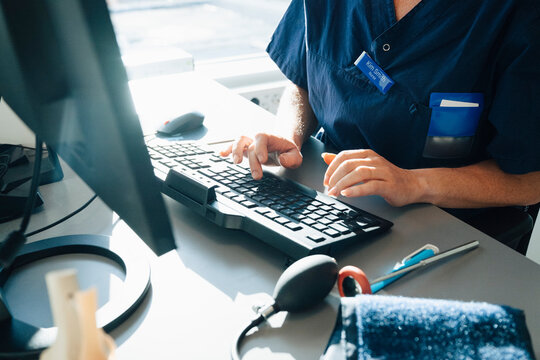 Midsection of female medical expert typing on keyboard while working in hospital office