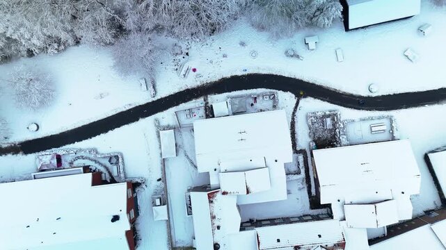 High-quality 4K 10-bit drone flyover above a snowy residential area surrounded by forest in the Netherlands during an early winter morning. Peaceful atmosphere, snow-covered rooftops, and stunning cin