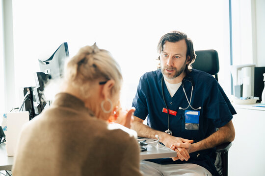 Male medical professional talking with sad senior woman in hospital room