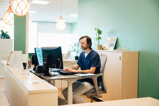 Focused male receptionist working on computer while sitting at desk in hospital building