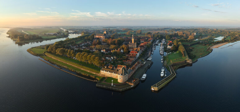 Aerial view of the historic town featuring the Grote Kerk, harbor with moored boats, and lush green embankments under a soft golden light Veere, Zeeland, Netherlands.