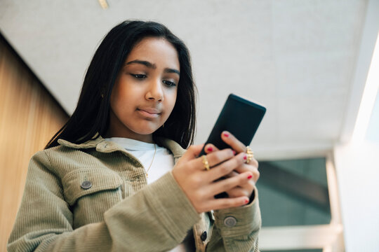 Low angle view of girl using smart phone while waiting for visit with doctor in medical clinic