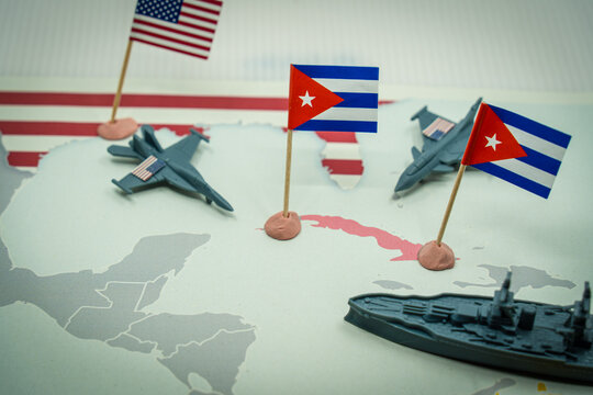 United States and Cuba flags on a world map with miniature jets and a battleship, symbolizing USA president Maximum Pressure Campaign on Cuba