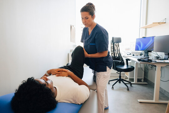 Female physiotherapist stretching leg of male patient lying on examination table in hospital