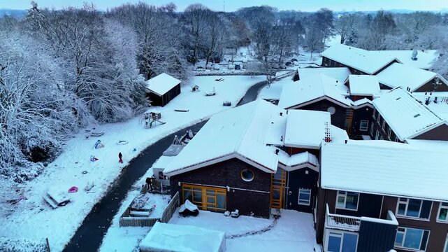 Beautiful 4K 10-bit aerial drone footage of a snow-covered housing estate located inside a winter forest in the Netherlands. Calm sunrise light, white snowy landscape, and cinematic winter atmosphere 