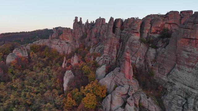 Close aerial pass along natural stone cliffs and rock pillars above dense autumn woodland.