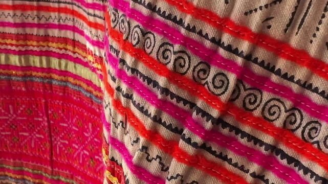 Close-up of vibrant embroidered fabric featuring intricate ethnic patterns in pink, red, and multicolor threads, with soft folds adding depth and texture to a rich cultural textile design.
