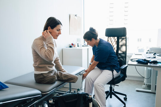 Amputee woman sitting on examination table during visit with female doctor in hospital room