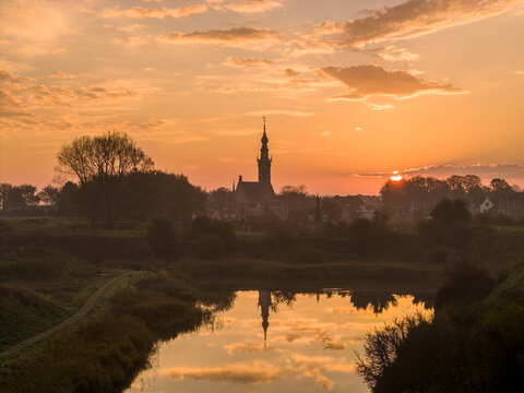 Aerial view of the historic town silhouette with the prominent church tower reflected in the calm water during a golden sunset Veere, Zeeland, Netherlands.