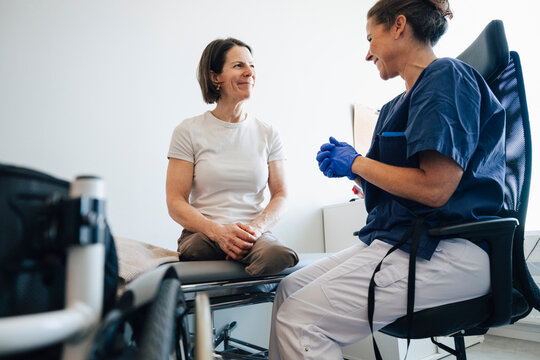Low angle view of smiling amputee woman talking with female healthcare expert in medical clinic