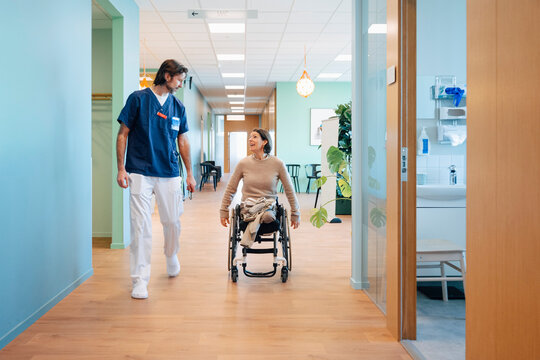 Full length of male medical professional talking with mature woman wheeling on wheelchair in hospital lobby