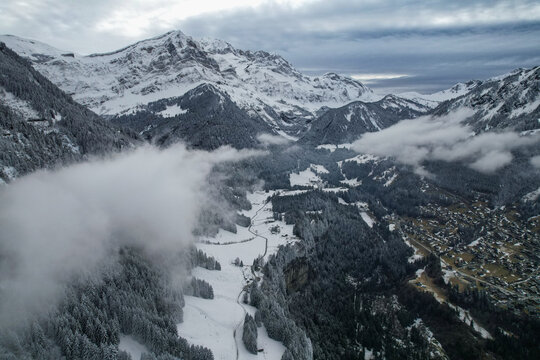 Aerial view of Les Rives and the snowy alpine valley with mist over pine forests and rugged peaks in Champery, Valais, Switzerland.