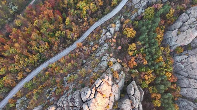 Overhead aerial view of a curving road through colorful autumn woodland and rocky terrain.
