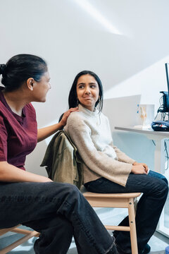 Mother consoling daughter while sitting on chair in doctor's office at hospital