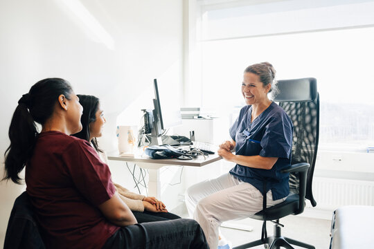 Smiling female pediatrician talking with mother and daughter while sitting in medical clinic