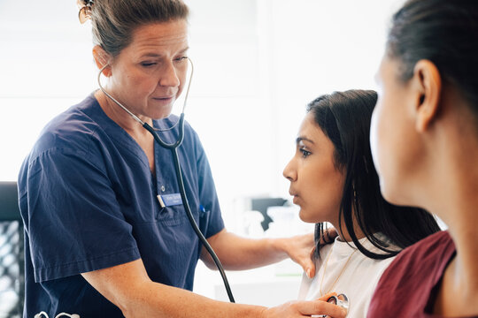 Female pediatrician listening to heartbeat of girl through stethoscope during medical exam in hospital
