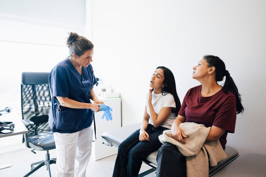 Mother sitting beside daughter showing neck problems to female healthcare expert in examination room at hospital