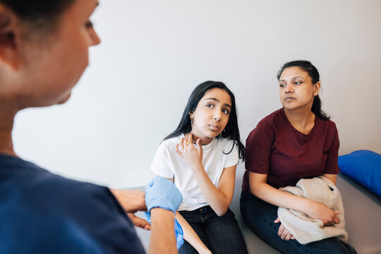 High angle view of mother sitting beside daughter showing neck problems to female healthcare expert in examination room