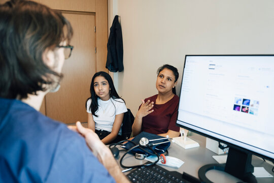 Woman explaining problems to male doctor while sitting with daughter in clinic