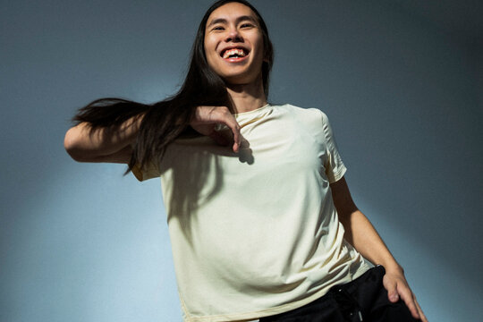 Low angle view of happy non-binary person dancing against colored background