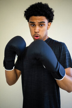 Portrait of young man with gloves posing in boxing stance against colored background