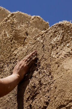 Hand shaping wet adobe wall during traditional earthen construction