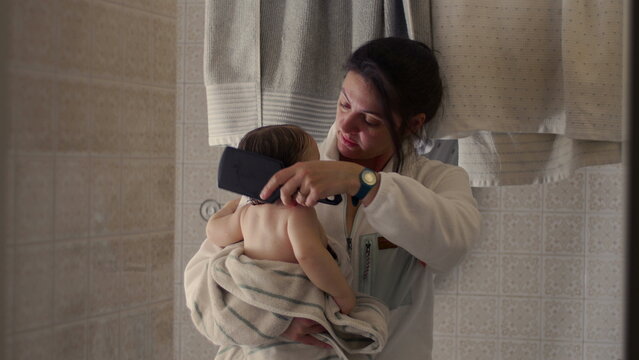 Mother brushing baby&rsquo;s wet hair while holding in towel after bath, nurturing family hygiene and bedtime care