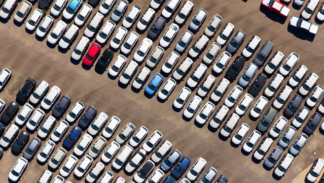 New cars are parked in parallel rows on an enormous outdoor lot, showcasing vehicle inventory management and the global automotive transportation industry supply chain from above