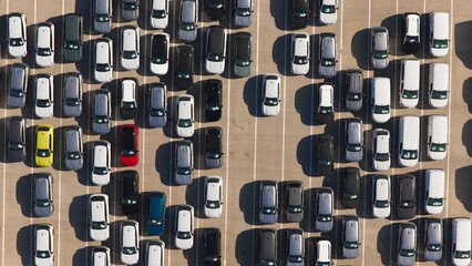 Rows of newly manufactured passenger vehicles and vans parked diagonally on a vast asphalt car lot, awaiting transportation and distribution to dealerships and consumers © Nasos Zovoilis